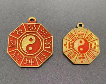 May include: Two octagonal pendants with a yin-yang symbol in the center. The pendants are red with gold-colored accents and Chinese characters around the edges. One pendant is slightly larger than the other.