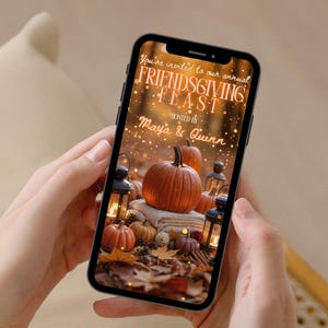May include: A smartphone displays a Friendsgiving invitation with pumpkins, lanterns, and fall foliage. The text reads "You're invited to our annual FRIENDS GIVING FEAST" hosted by Maya & Quinn.