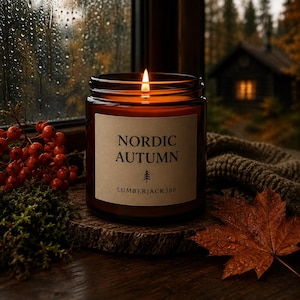 Puede incluir: Una vela encendida en un frasco de vidrio marrón con una etiqueta beige que dice NORDIC AUTUMN y LUMBERJACK350, con un icono de árbol. La vela descansa sobre una rodaja de madera junto a bayas rojas, musgo verde y una hoja de arce marrón.