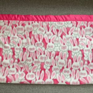 Fleece baby or toddler blanket in a pattern of cute white bunnies on a pink background, with pink satin trim