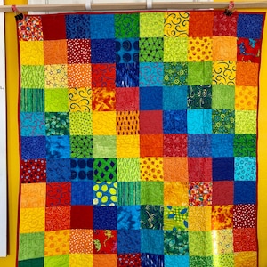 May include: A colorful patchwork quilt with a rainbow pattern. Each square is a different fabric with a unique design. The quilt is made up of red, orange, yellow, green, blue, indigo, and violet squares.