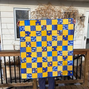 May include: A blue and yellow patchwork quilt with a space theme. The quilt is made up of squares with different space-themed patterns, including stars, planets, and moons.