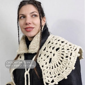 May include: Cream-coloured crochet shawl with an openwork design. The shawl is worn over a black jacket with a cream-coloured shearling collar. Text on the image reads "CROCHET PATTERN PDF + VIDEO TUTORIAL".