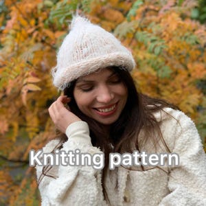 May include: A knitted white hat with a pointed top and a rolled brim. The hat is made of a soft, textured yarn. The text "Knitting pattern" is displayed in white letters at the bottom of the image.