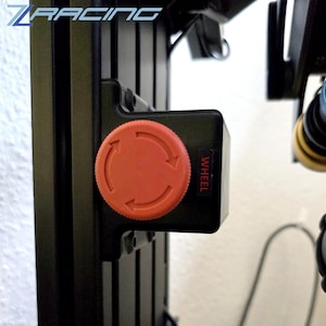 May include: Close-up of a black component with an orange dial featuring directional arrows. The word "WHEEL" is printed vertically in white. The logo "Z RACING" is visible in the upper left corner. The component is mounted on a black frame.