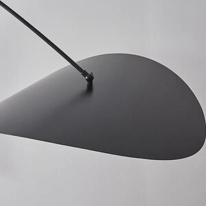 May include: A modern, minimalist black pendant light fixture. The design features a large, teardrop-shaped shade suspended from a thin, angled arm. The fixture is made of metal and has a matte finish, creating a sleek and contemporary aesthetic.