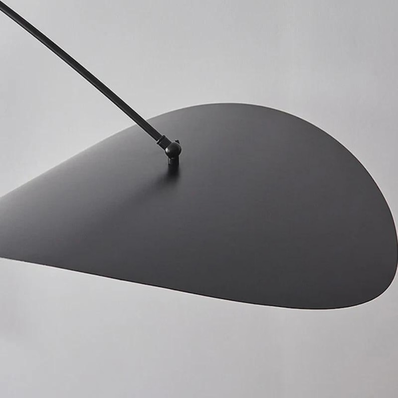 May include: A modern, minimalist black pendant light fixture. The design features a large, teardrop-shaped shade suspended from a thin, angled arm. The fixture is made of metal and has a matte finish, creating a sleek and contemporary aesthetic.
