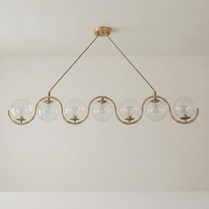 May include: A modern, gold-toned chandelier with six clear glass globe shades. The fixture has a wavy design and is suspended from the ceiling by two thin wires. The light bulbs are visible inside the globes.