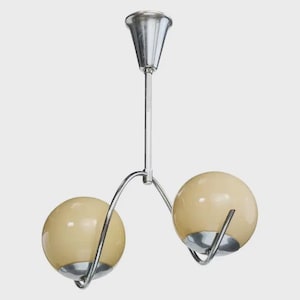 May include: A vintage two-light chandelier with a chrome finish. The fixture features two cream-colored globe shades and a central stem. The shades are held by curved metal arms, creating a mid-century modern aesthetic.