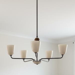 May include: A modern chandelier with five off-white, tulip-shaped glass shades. The fixture has a dark brown metal frame and a central stem. The light hangs from the ceiling, providing ambient lighting.
