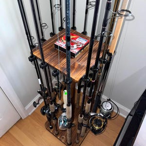 May include: A wooden fishing rod rack with multiple fishing rods of varying lengths and colors. The rack has a dark wood finish and a square top. A box of fishing line is visible on the top shelf.