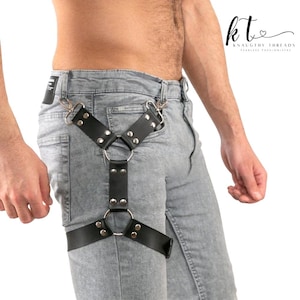 May include: Black leather harness with silver metal hardware. The harness has a Y-shaped design with adjustable straps and a thigh band. The brand name "KNAUGHTY THREADS" is visible in the upper right corner.
