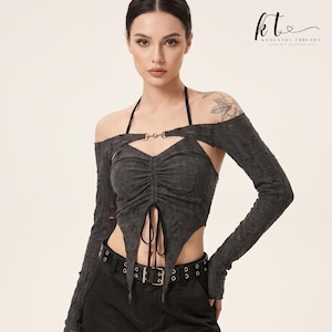Op de afbeelding: Een donkergrijze, distressed top met lange mouwen, een halterhalslijn, een centrale metalen ringverbinding en een geplooid lijfje met twee hangende stoffen linten. Het kledingstuk heeft een korte, puntige zoom en off-shoulder mouwen met gaten.