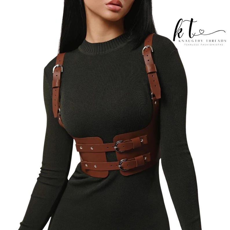 May include: Brown leather harness with silver buckles and straps. The harness has a chest plate and two waist straps. The text "kt" and "KNAUGHTY THREADS FEARLESS FASHIONISTAS" is in the upper right corner.