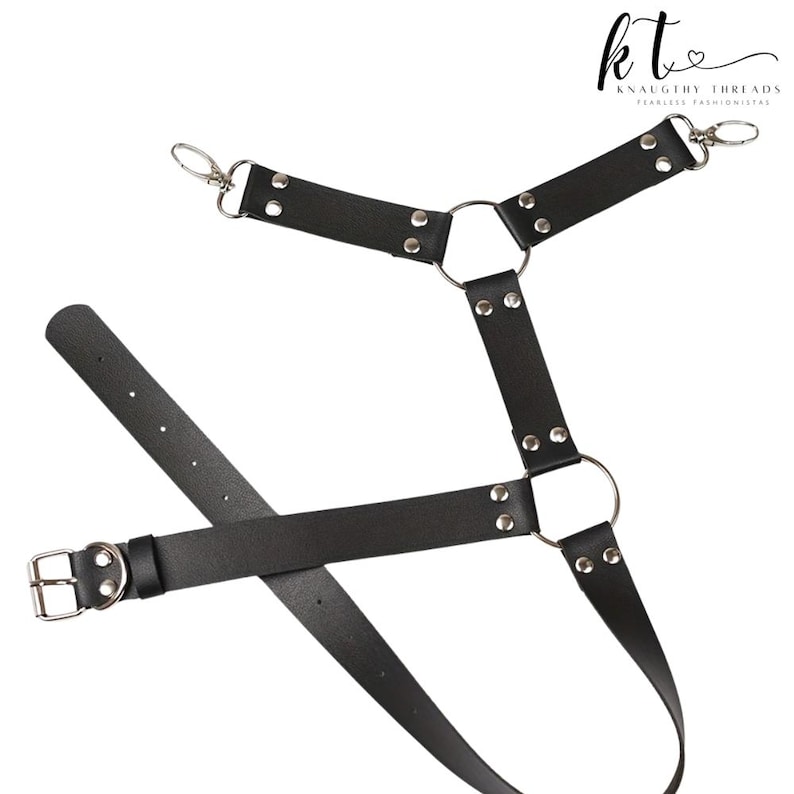 May include: Black leather harness with silver metal hardware, including rings, rivets, and clasps. The harness features adjustable straps and a buckle closure. The brand name "Knaughty Threads" is visible in the upper right corner.