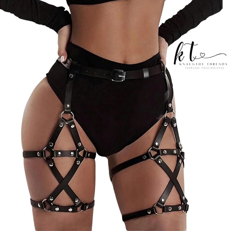 May include: Black leather body harness with a belt and leg straps. The harness features metal rings and studs, with a star-like design on the leg straps. The brand name "KNAUGHTY THREADS" is visible in the upper right corner.