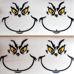 May include: Four stickers featuring the Grinch's face. Each sticker has a white background with a black outline of the Grinch's face, including his eyebrows, eyes, and smile. The eyes are yellow.