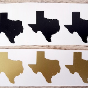 Può includere: Sei adesivi raffiguranti lo stato del Texas. Tre sono neri e tre dorati. Gli adesivi sono fustellati a forma di stato, con sfondo bianco.
