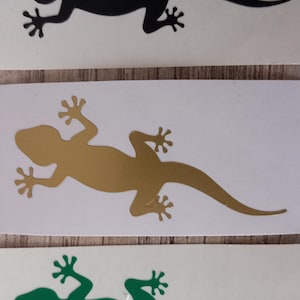 Könnte beinhalten: Drei Eidechsen-Aufkleber in Schwarz, Gold und Grün. Jeder Aufkleber ist eine Silhouette einer Eidechse mit detaillierten Füßen und einem langen Schwanz. Die Aufkleber werden auf weißem Hintergrund angezeigt.