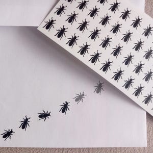 May include: White envelope and card with a pattern of black ant illustrations. The ants are arranged in rows on the card and in a line on the envelope, creating a unique design. The image is a close-up shot.