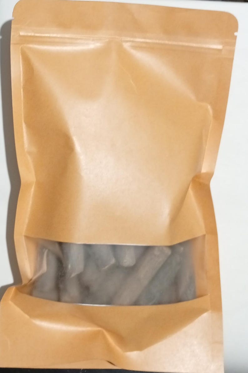 Pode incluir: Uma sacola de papel marrom com uma janela transparente, selada com um z&iacute;per. A janela revela uma cole&ccedil;&atilde;o de objetos cil&iacute;ndricos cinzentos. A sacola &eacute; feita de papel marrom claro.