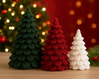 Könnte beinhalten: Drei handgefertigte gehäkelte Weihnachtsbäume in Grün, Rot und Weiß. Die Bäume stehen auf einer Holzoberfläche mit einem verschwommenen Hintergrund aus Weihnachtslichtern und einem roten Hintergrund. Die Bäume sind unterschiedlich groß.