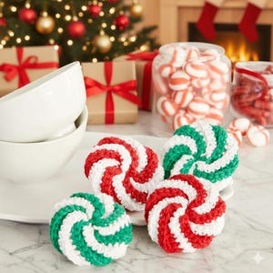 May include: A festive holiday scene featuring crocheted spiral ornaments in red, white, and green. The ornaments are arranged on a white plate, with jars of candy and wrapped gifts in the background. A Christmas tree with lights and ornaments is also visible.