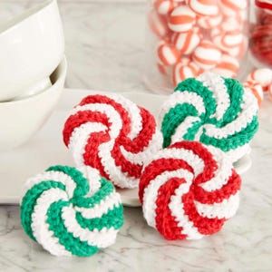Puede incluir: Cuatro posavasos de ganchillo hechos a mano con un dise&ntilde;o en espiral. Dos posavasos son rojos y blancos, y dos son verdes y blancos. Los posavasos est&aacute;n sobre un plato blanco, con un tarro de caramelos rojos y blancos en el fondo.