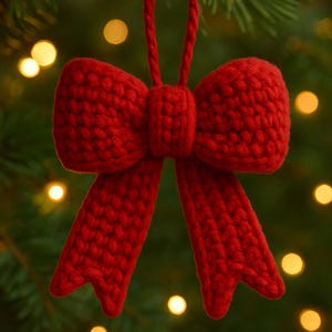 Puede incluir: Adorno navideño de lazo rojo tejido a mano. El lazo, con textura, presenta un nudo central y dos lazos colgantes. Se suspende de un cordón rojo a juego, ideal para la decoración festiva. Fondo con luces borrosas.
