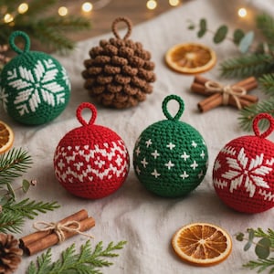May include: A set of five crocheted ornaments including three spherical balls with white geometric patterns in red and green, one brown textured pinecone-shaped ornament, and one green ball with a white snowflake design, each with a loop.