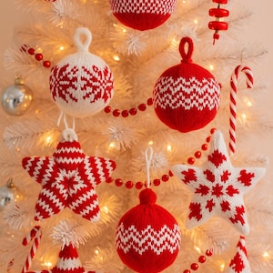 Puede incluir: Un árbol de Navidad blanco adornado con adornos de punto rojos y blancos. Las decoraciones incluyen adornos en forma de estrella y redondos, junto con acentos de bastones de caramelo y guirnaldas de cuentas rojas. Luces blancas cálidas iluminan la escena.