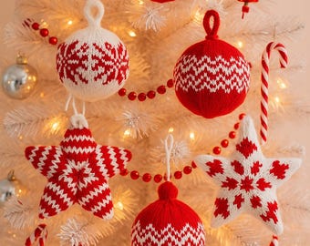 Puede incluir: Un árbol de Navidad blanco adornado con adornos de punto rojos y blancos. Las decoraciones incluyen adornos en forma de estrella y redondos, junto con acentos de bastones de caramelo y guirnaldas de cuentas rojas. Luces blancas cálidas iluminan la escena.