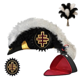 Puede incluir: Un sombrero ceremonial negro y blanco con un emblema y ribete dorados, y un manojo de plumas negras y blancas. El sombrero tiene un interior rojo y se muestra con un emblema a juego.