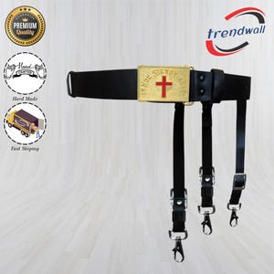 May include: Black leather belt with a gold-colored buckle featuring a red cross and text. The belt has three black straps with metal clasps. The image also includes logos for "Premium Quality", "Hand Crafted", and "Fast Shipping".
