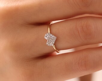 May include: A gold ring featuring a heart-shaped design encrusted with small, sparkling stones. The ring's band is a thin, polished gold, and the heart is composed of numerous tiny, clear gemstones. The ring is shown on a person's finger.