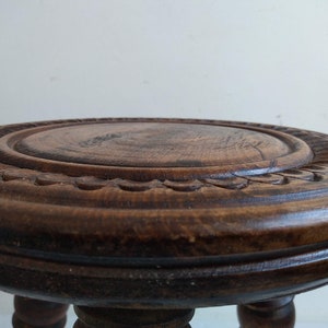 May include: A dark brown wooden stool with a carved top and three legs.