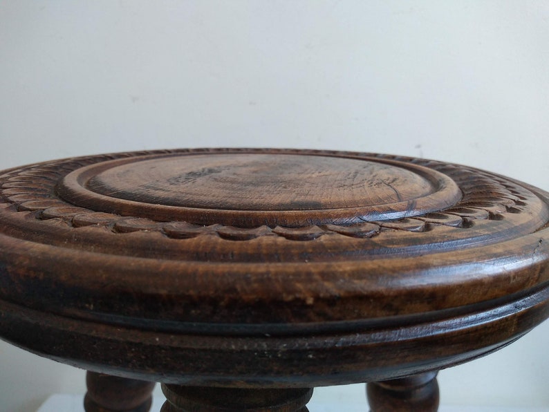 May include: A dark brown wooden stool with a carved top and three legs.