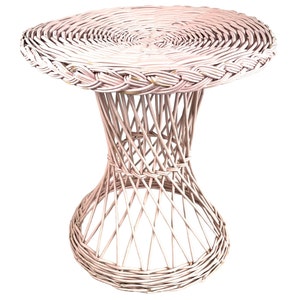 May include: A light pink wicker side table with a round top and hourglass-shaped base. The table is made of woven wicker, with a braided edge on the tabletop. The base has a woven, open design. The table is suitable for indoor or outdoor use.