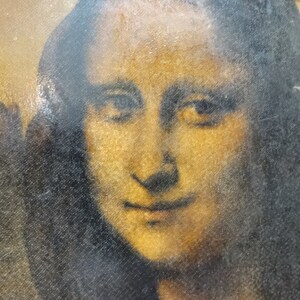 Puede incluir: Un primer plano de una pintura de la cara de una mujer. La mujer tiene el pelo oscuro y una sonrisa suave. La pintura est&aacute; ligeramente descolorida y tiene una superficie texturizada.