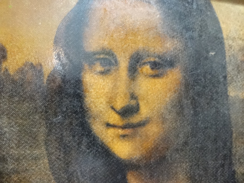 Puede incluir: Un primer plano de una pintura de la cara de una mujer. La mujer tiene el pelo oscuro y una sonrisa suave. La pintura est&aacute; ligeramente descolorida y tiene una superficie texturizada.