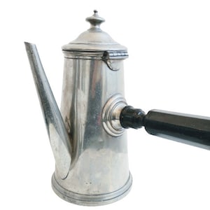 Peut inclure: Une cafetière en argent avec une poignée en bois noir. La cafetière a un corps arrondi et un bec verseur sur le côté. La poignée est fixée sur le côté de la cafetière.