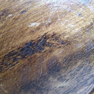 May include: Close-up of a dark brown wooden surface with a smooth, polished finish. The surface shows signs of wear and tear, with scratches and marks visible.