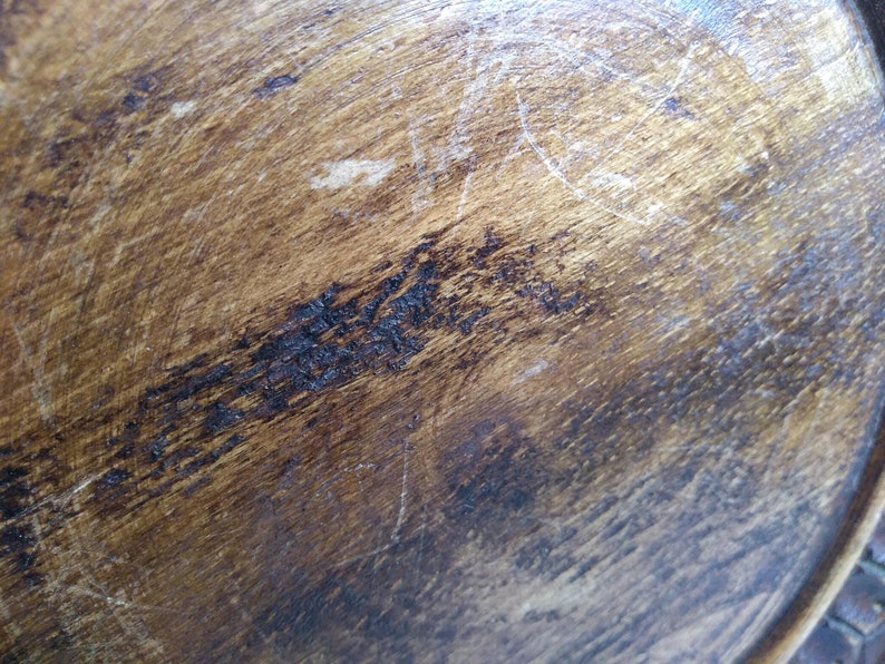 May include: Close-up of a dark brown wooden surface with a smooth, polished finish. The surface shows signs of wear and tear, with scratches and marks visible.