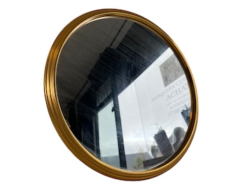Peut inclure: Un miroir rond avec un cadre doré et une surface réfléchissante. Le miroir est incliné et reflète l'intérieur d'un magasin avec le texte "Antiquites & Curios ACHA" et un numéro de téléphone.