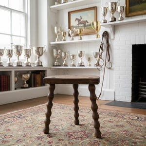 Può includere: Uno sgabello in legno marrone scuro con una seduta triangolare liscia e piatta e tre gambe distintive in stile bobina. Lo sgabello presenta un design in legno tornito con segmenti arrotondati e impilati su ogni gamba, offrendo una base solida.