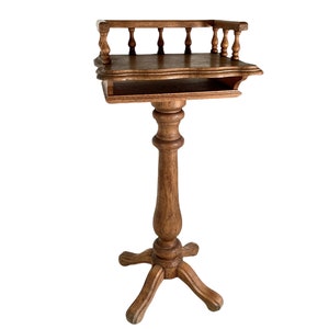 May include: A wooden stand with a single shelf and a decorative railing. The stand has a turned pedestal and a four-legged base.