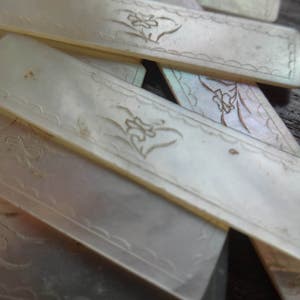 Puede incluir: Un juego de seis marcapáginas de nácar blanco con un diseño floral. Los marcapáginas son rectangulares y tienen una superficie lisa y pulida.