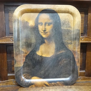 Puede incluir: Una bandeja de madera vintage con una imagen impresa de la Mona Lisa. La bandeja tiene un marco de madera marr&oacute;n y un aspecto ligeramente desgastado.