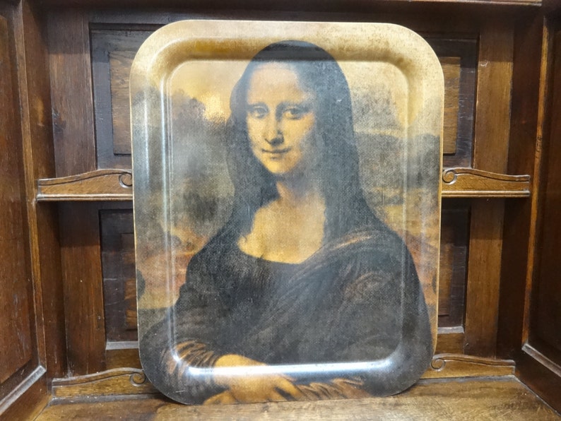 Puede incluir: Una bandeja de madera vintage con una imagen impresa de la Mona Lisa. La bandeja tiene un marco de madera marr&oacute;n y un aspecto ligeramente desgastado.