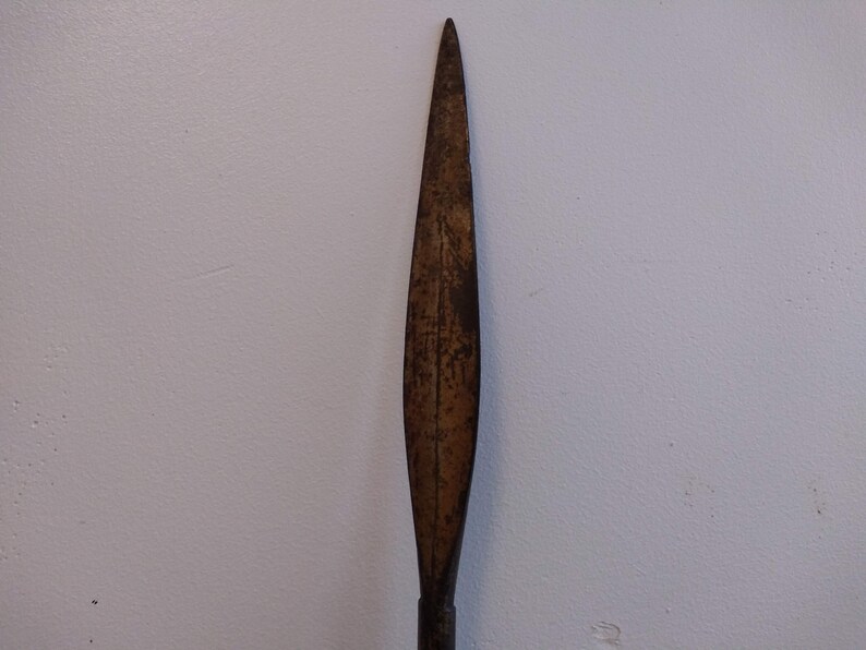 May include: A long, narrow, rusty metal spearhead with a pointed tip.